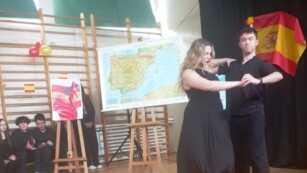 Zdjęcie przedstawia parę tańczącą, po lewej stronie siedzą uczniowie, za parą tańczącą widoczna mapa Hiszpanii i wystrój sceny na styl hiszpański